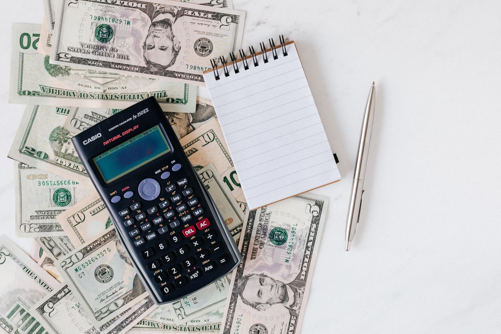 A calculator and notepad on a desk with US dollar bills, for working out balance transfer fee math.